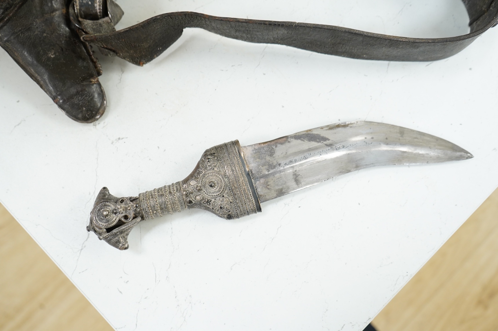A late 19th century Arab silver mounted dagger jambya with silver filigree mounts to hilt and sheath, in its leather covered scabbard with parts of the original belt